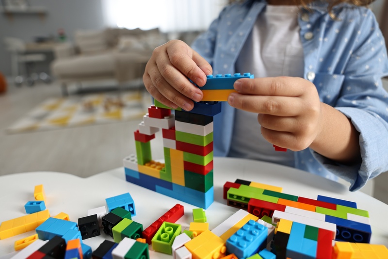 Girl playing with building blocks at white table indoors, closeup. Selective focus