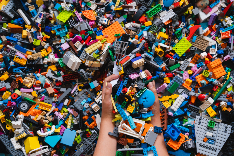 Huge pile of mixed colorful plastic bricks toys with children's hands. Small plastic building blocks in multiple colours, top view, lifestyle photo. Kids leisure, children education and development.